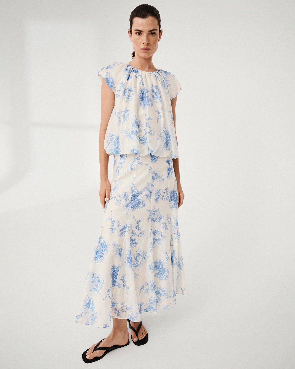 Model wearing a white and blue floral top and skirt on a light grey background
