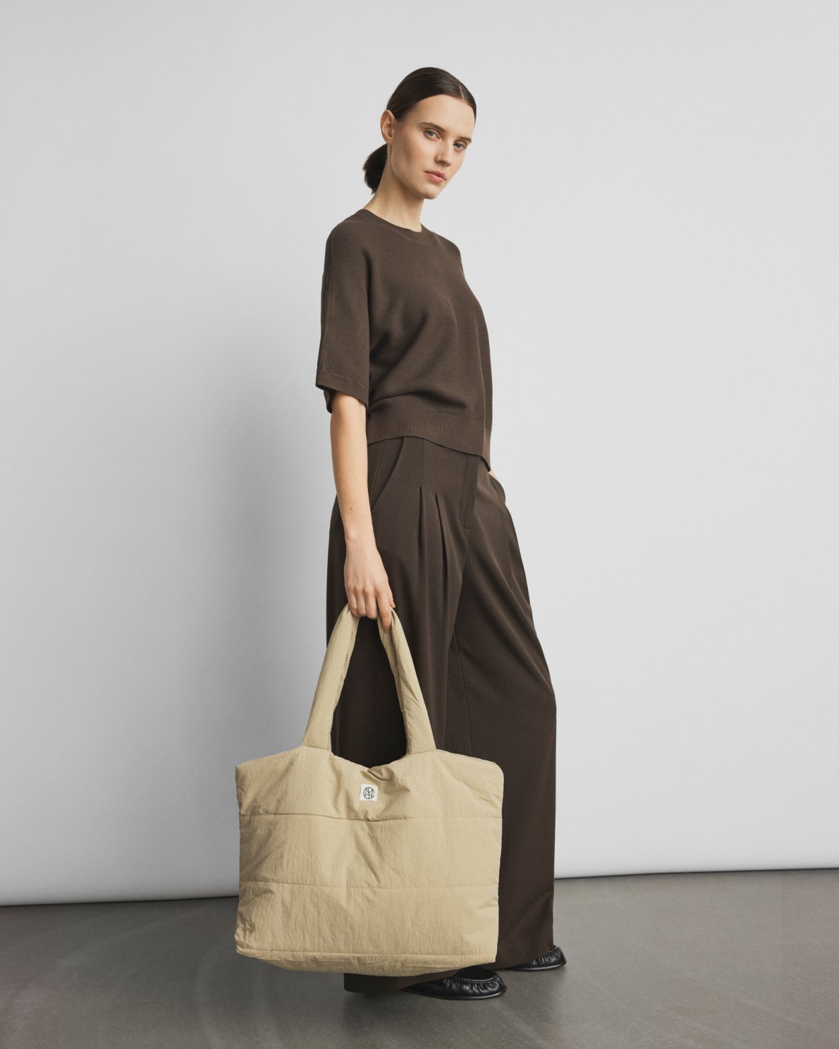 Woman holding a beige tote bag against a plain background