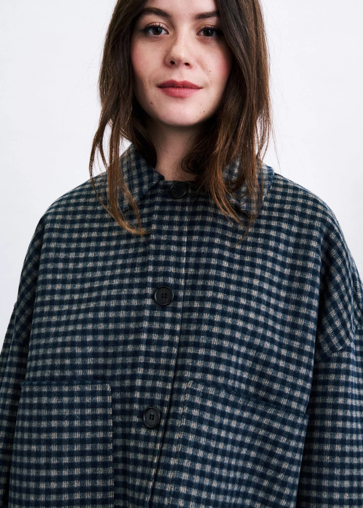A woman wearing a dark navy and gray gingham button-up shirt jacket, shown from the chest up against a plain white background.