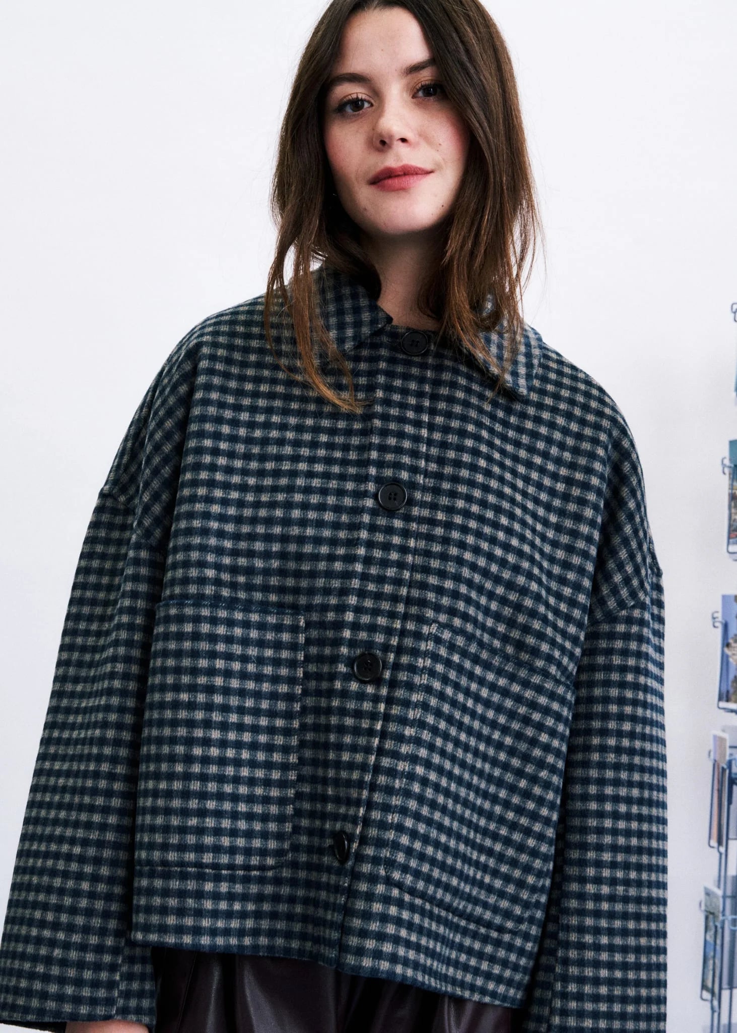 A woman wearing a dark navy and gray gingham patterned button-up jacket, photographed against a plain white wall.