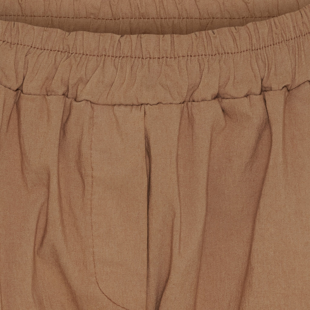 Close-up of a pair of brown trousers showing the elastic waistband and pleated fabric texture.