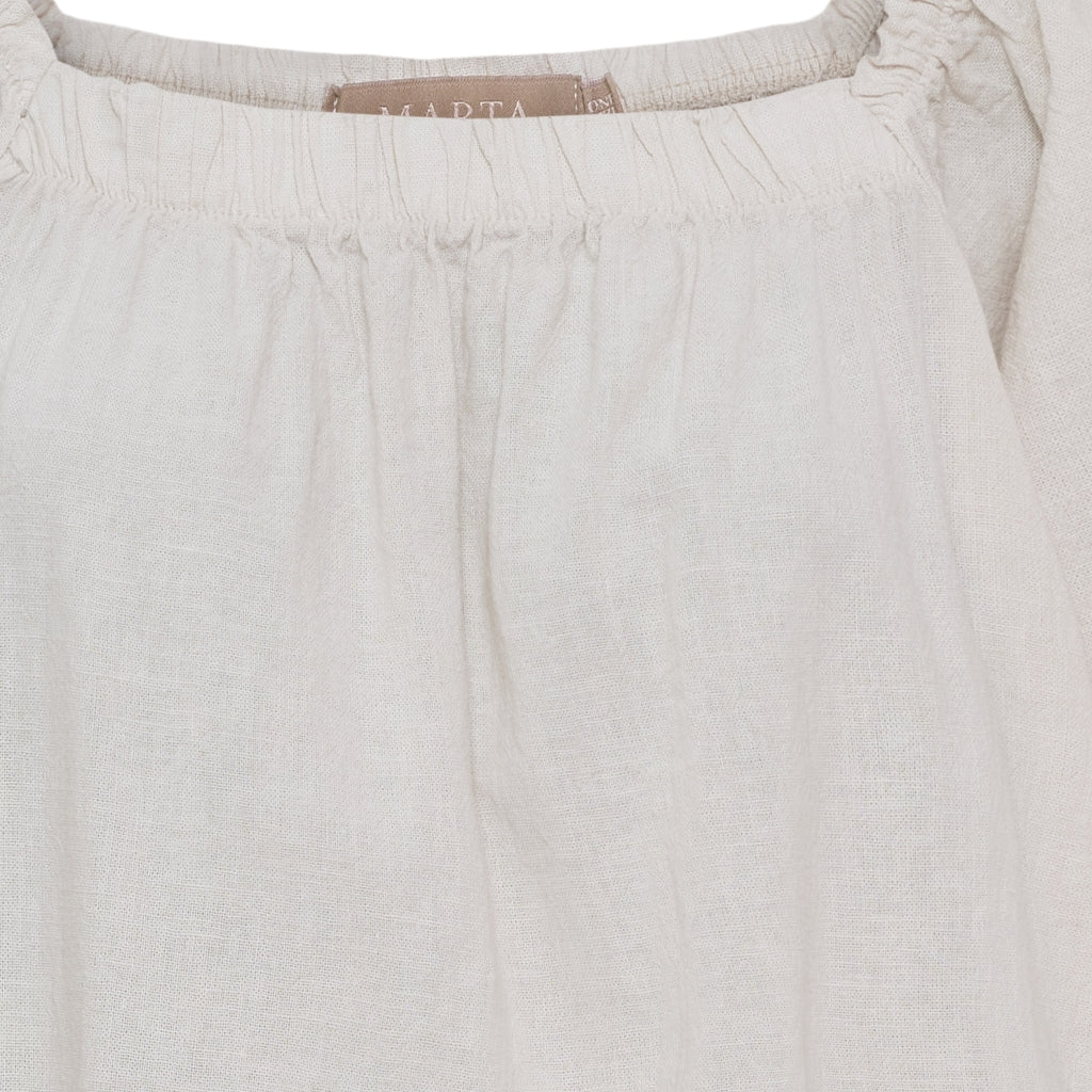 Close-up of light gray pants with a brand label on a white background
