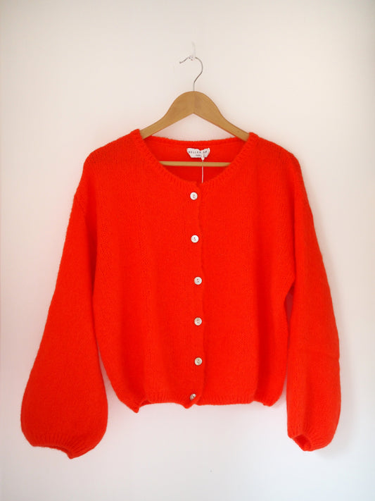 Orange Red cardigan on a wooden hanger against a white background