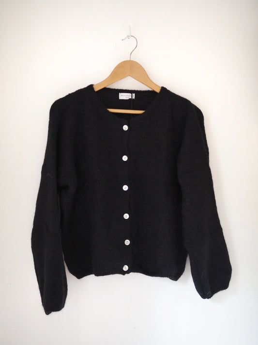 Black cardigan on a wooden hanger against a white background