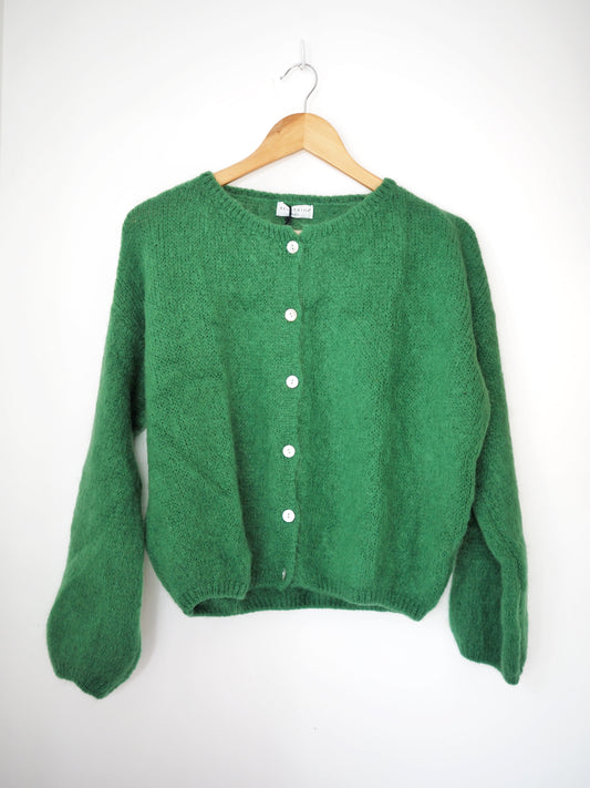 Green cardigan on a wooden hanger against a white background