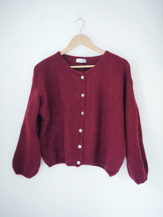 Maroon cardigan on a wooden hanger against a white background