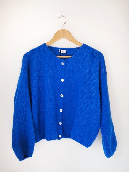 Blue cardigan on a wooden hanger against a white background