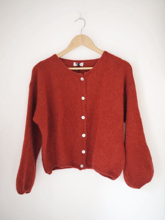 Red cardigan on a wooden hanger against a white background