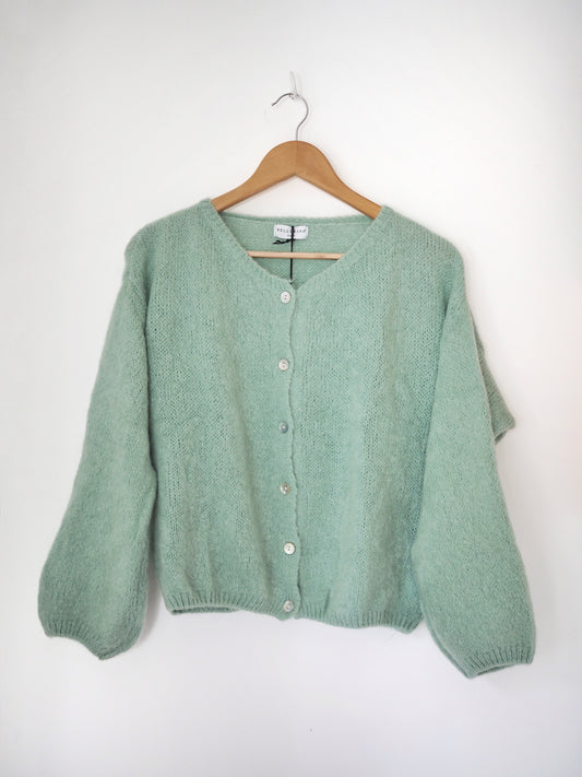 Mohair cardigan in mint green hanging on a wooden hanger on a white background