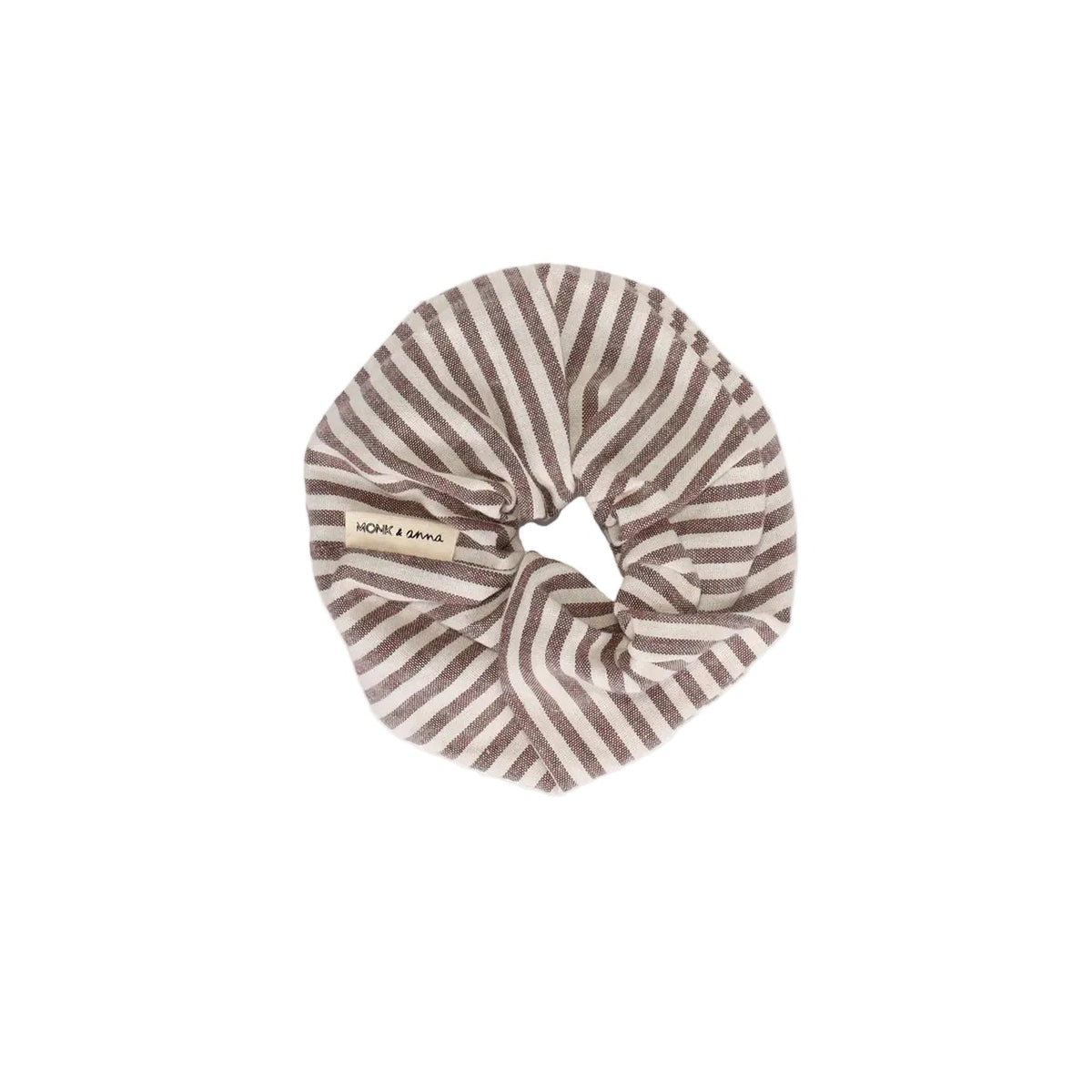 A fabric hair scrunchie with a brown and beige horizontal stripe pattern, featuring a small woven brand label that reads 'COCO + CARMEN'. The product is photographed flat against a solid off-white background.