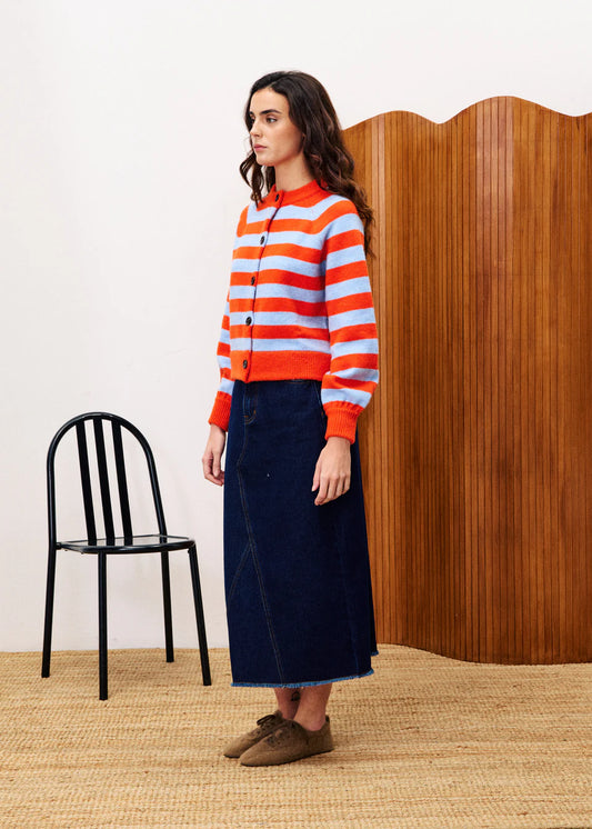 Woman wearing a red and blue striped sweater with a black chair and wooden panel in the background.