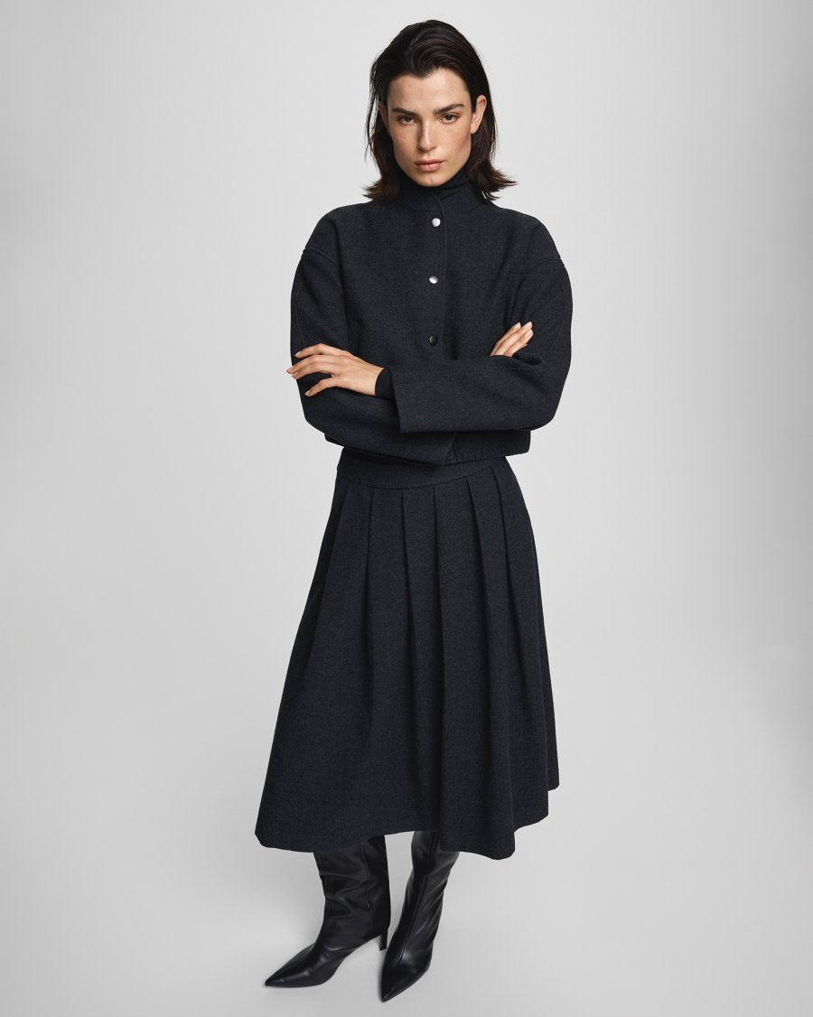 Woman wearing a black outfit with a long skirt and boots on a light gray background