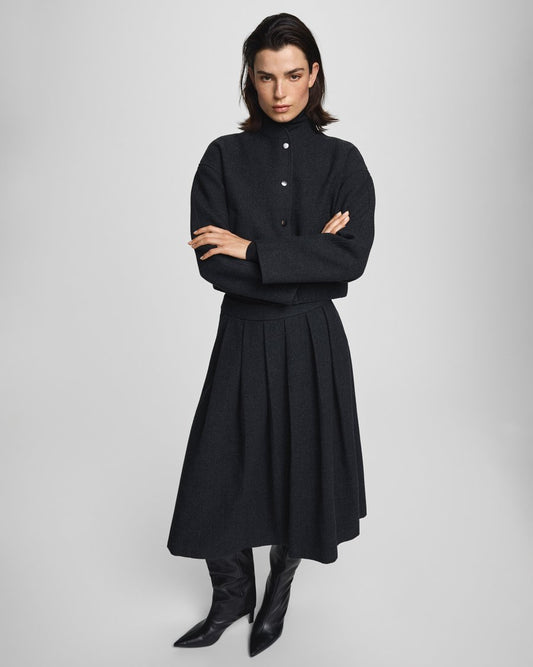 Woman wearing a black outfit with a long skirt and boots on a light gray background