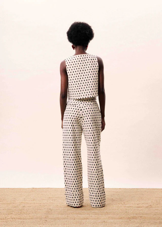 Person wearing a patterned sleeveless top and pants on a plain background