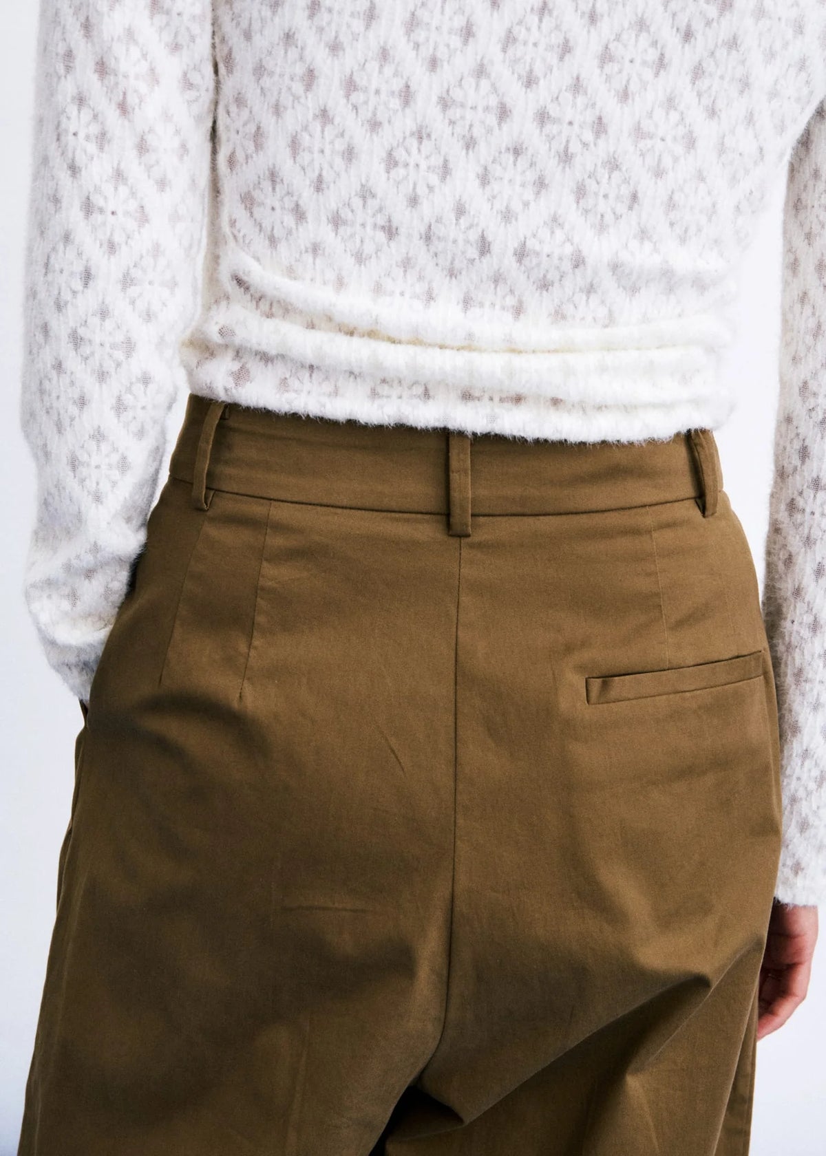 Close-up of a person wearing olive brown trousers and a white textured knit sweater, focusing on the back waistband and pocket area.