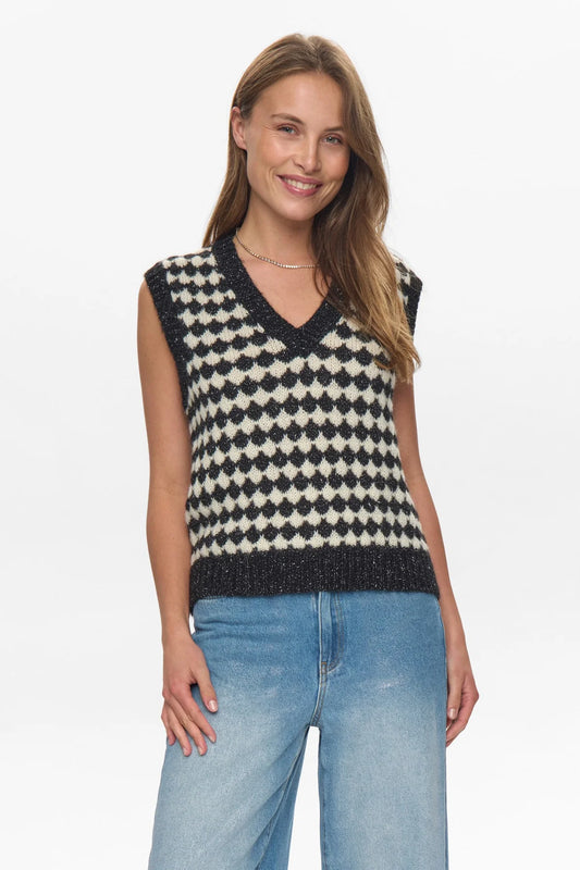 Woman wearing a black and white patterned sleeveless top with blue jeans on a white background