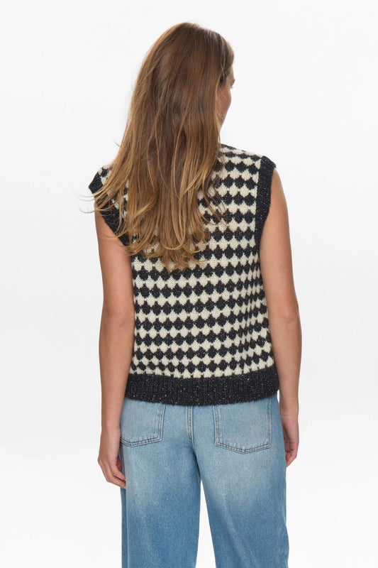 Person wearing a black and white patterned sleeveless top with blue jeans on a white background