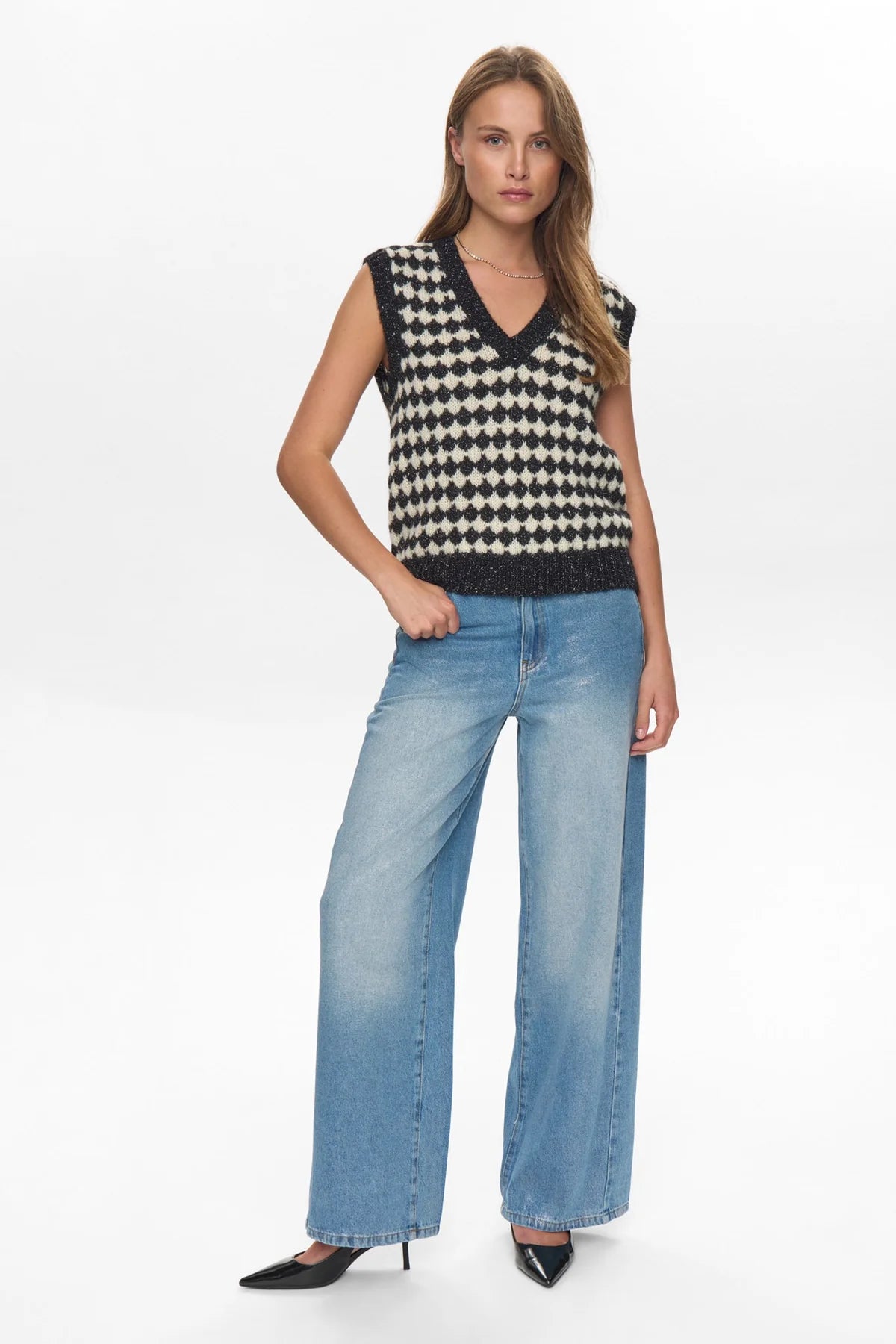 Woman wearing a black and white checkered sleeveless top and blue jeans on a white background