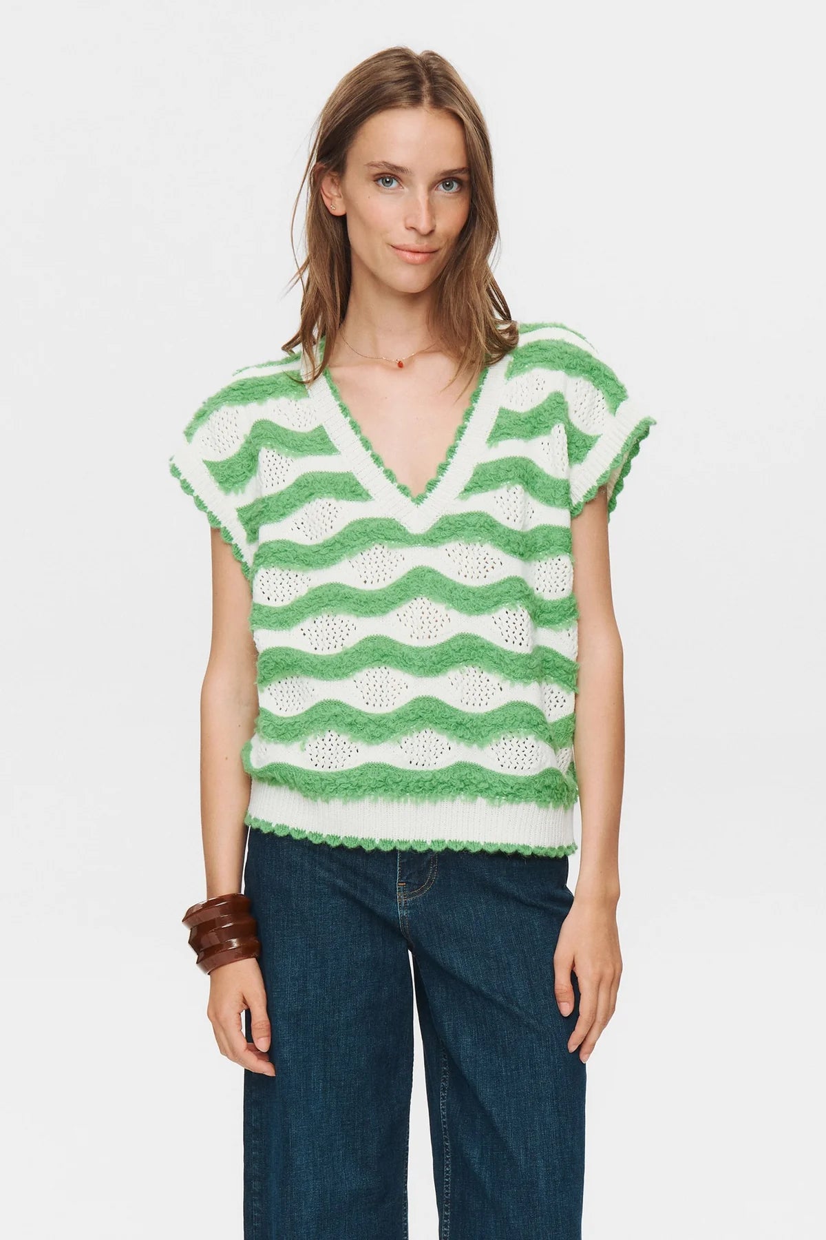 Woman wearing a green and white patterned sleeveless top with blue jeans on a white background