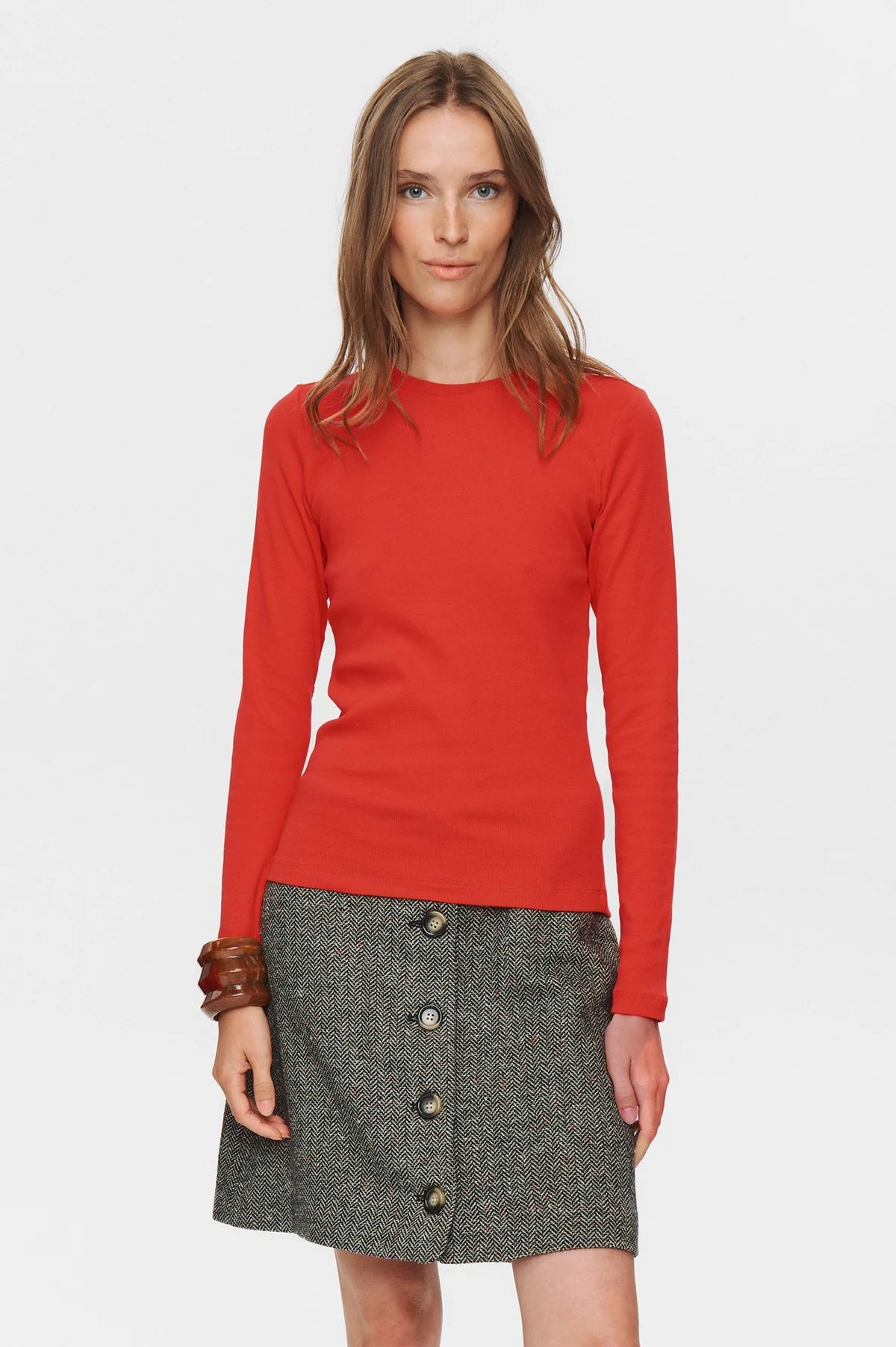 Woman wearing a red long-sleeve top and gray skirt with buttons on a white background