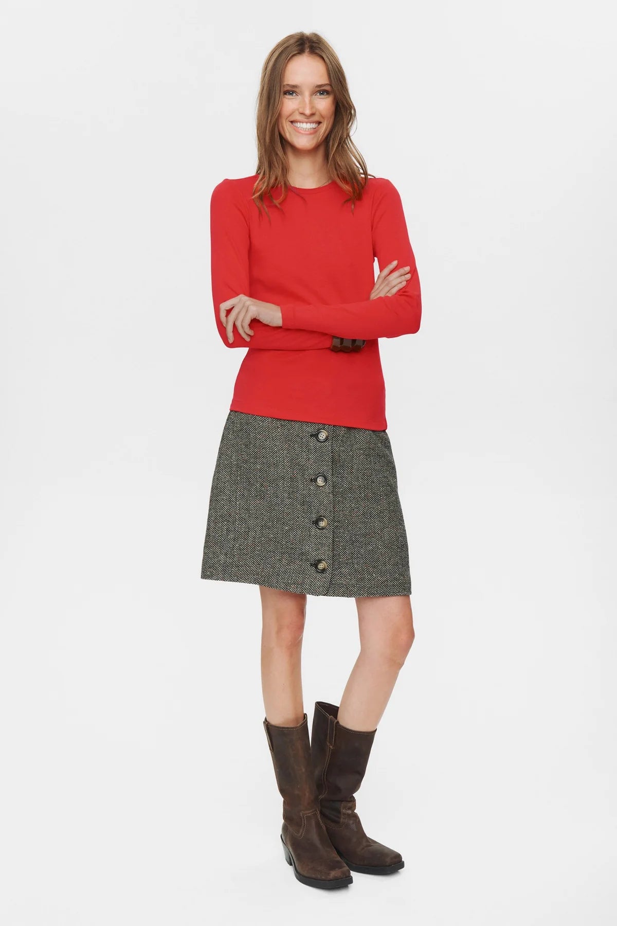 Woman wearing a red sweater and gray skirt with buttons on a white background