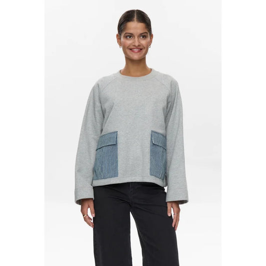 Woman wearing a gray sweater with denim pocket details on a white background