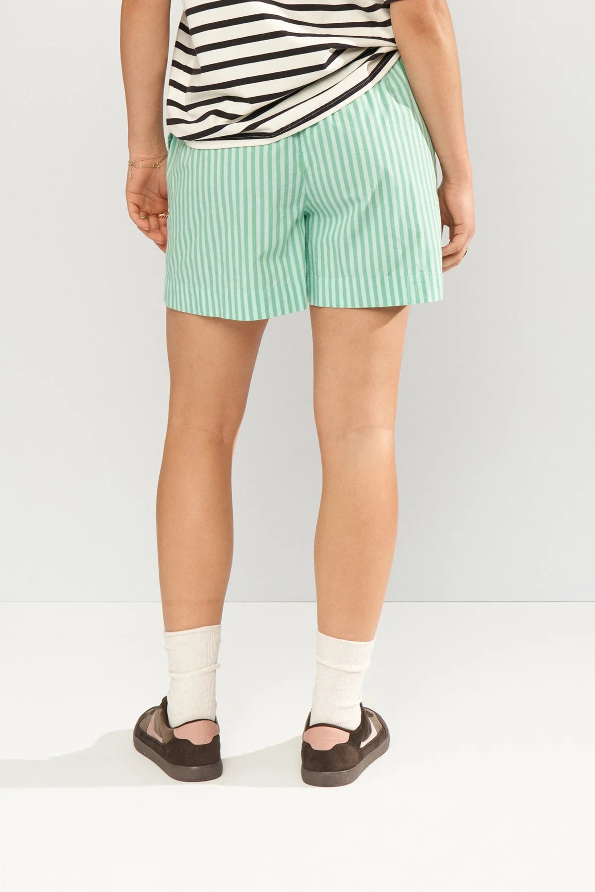 Person wearing green striped shorts and a black and white top on a white background