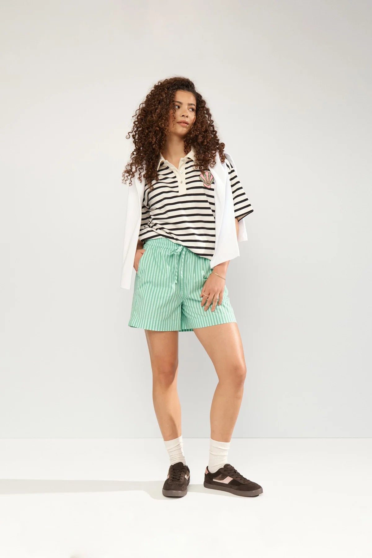 Woman wearing a striped shirt, green shorts, and black shoes on a white background