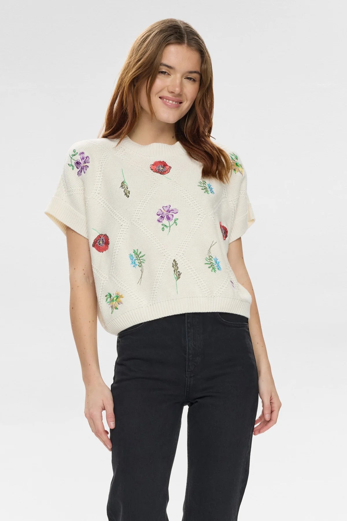 Woman wearing a cream-colored t-shirt with floral embroidery on a plain background