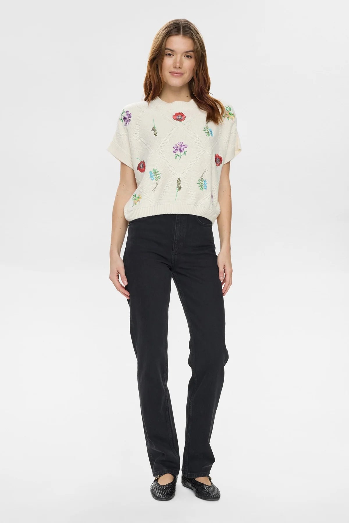 Woman wearing a cream-colored blouse with floral patterns and black pants on a white background