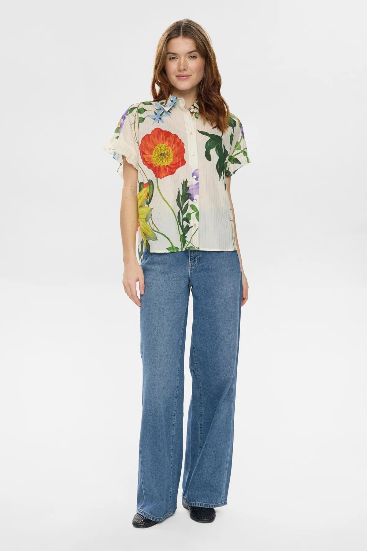 Woman wearing a Floral short sleeve blouse with floral detail with blue jeans on a white background