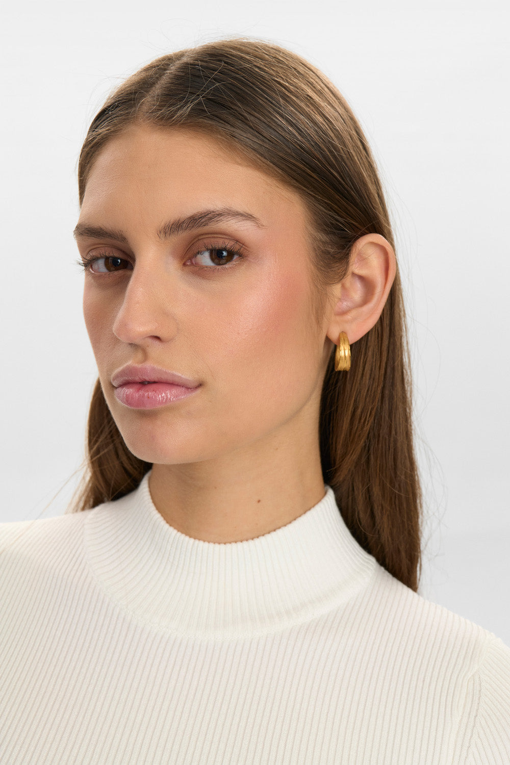 Woman wearing gold earrings against a plain background