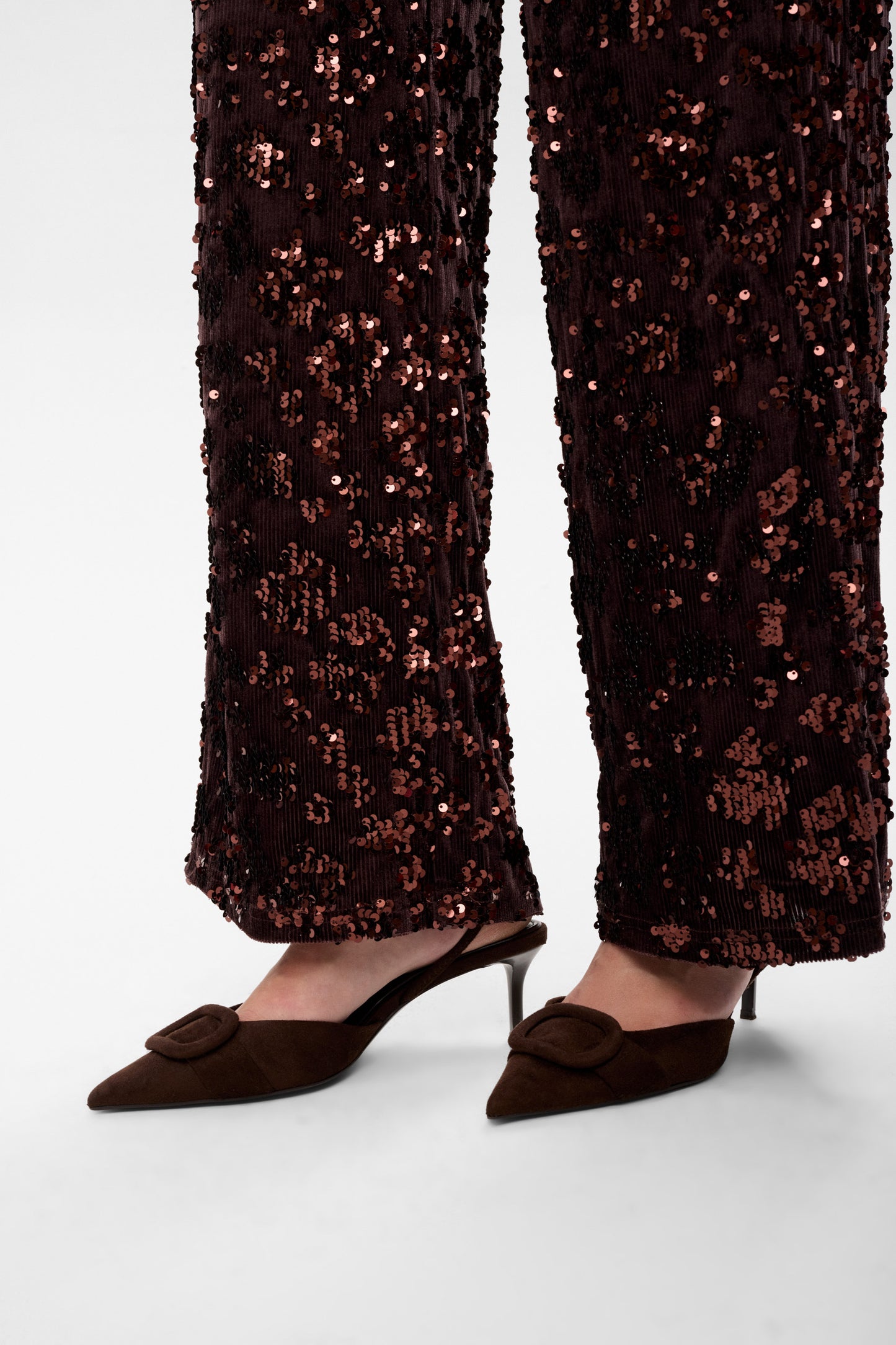 Person wearing black sequin pants and brown pointed-toe shoes on a white background