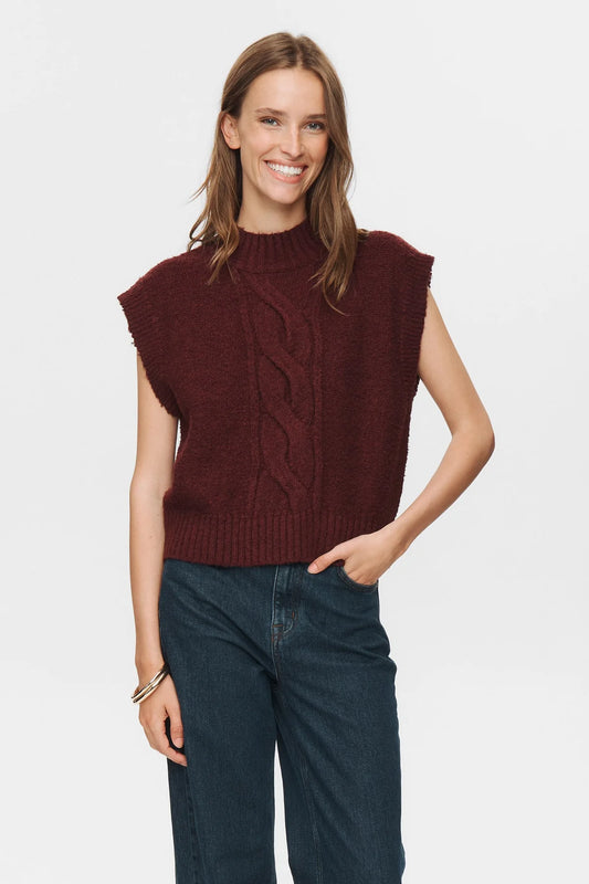 Woman wearing a burgundy knitted vest and blue jeans on a white background