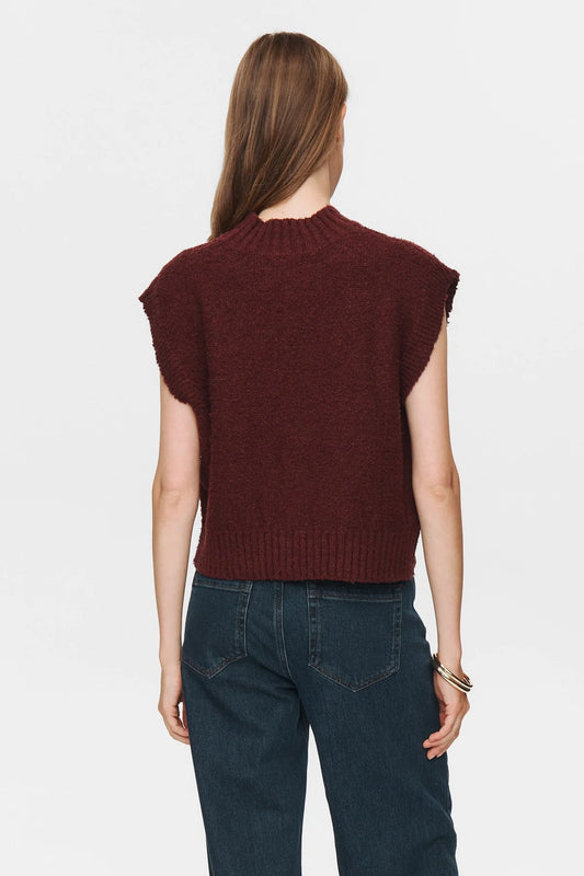 Person wearing a brown sleeveless sweater and blue jeans on a white background