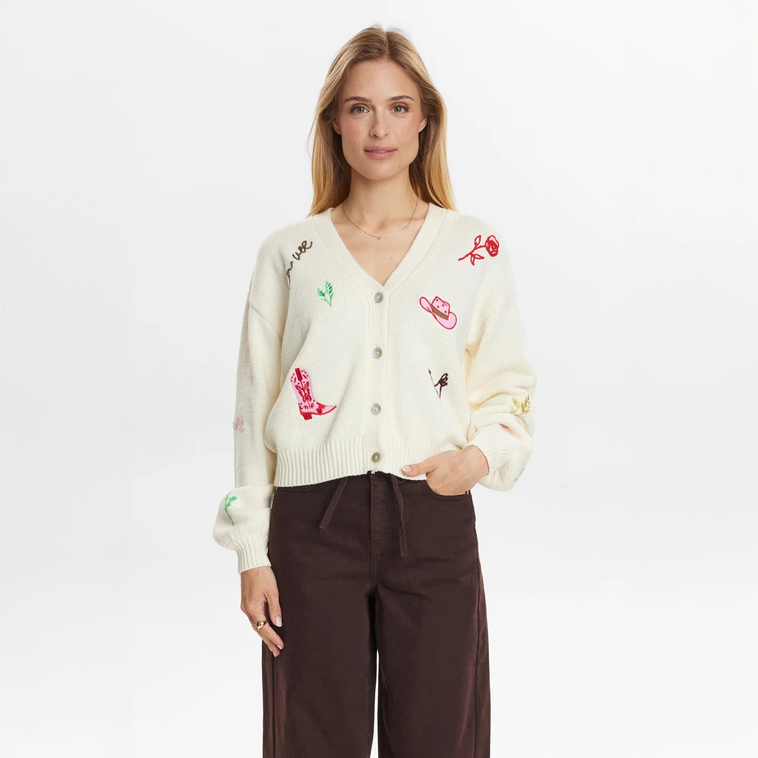 Woman wearing a cream cardigan with colorful embroidery on a white background