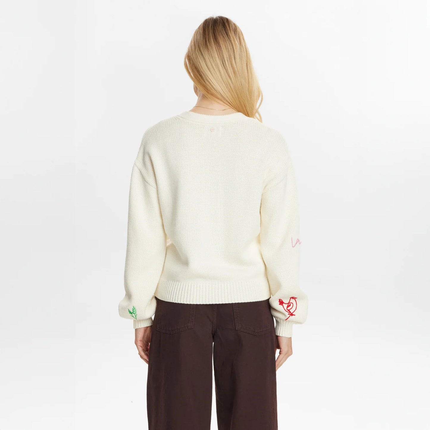 Person wearing a cream sweater with embroidered designs on a white background