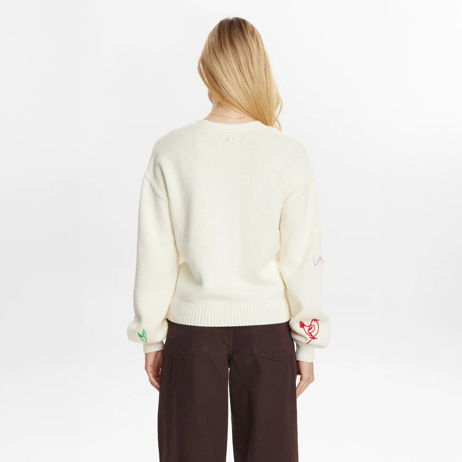 Person wearing a cream sweater with embroidered designs on a white background