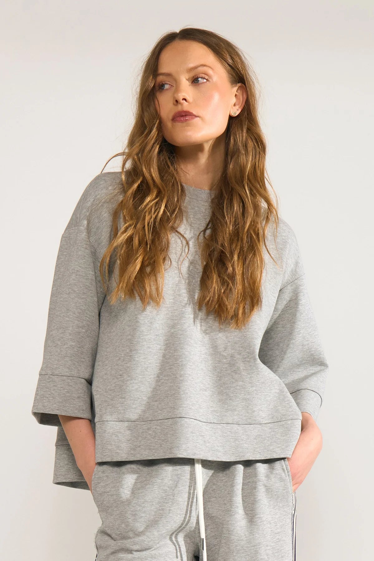 Woman wearing a gray sweatshirt and pants against a plain background