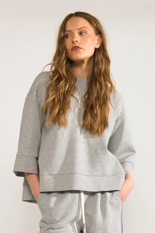 Woman wearing a gray sweatshirt and pants against a plain background