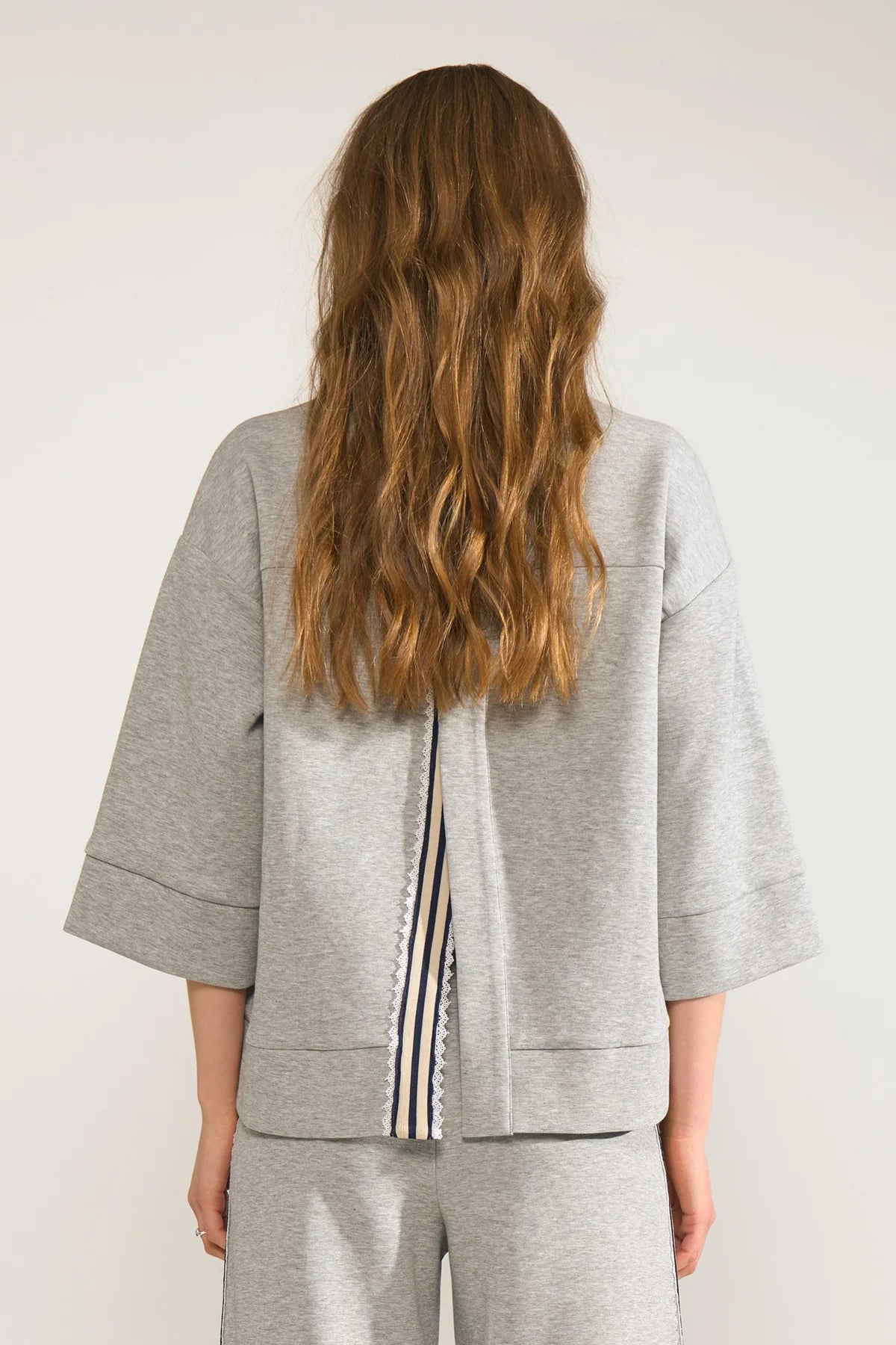 Person wearing a gray outfit with a striped detail on a white background