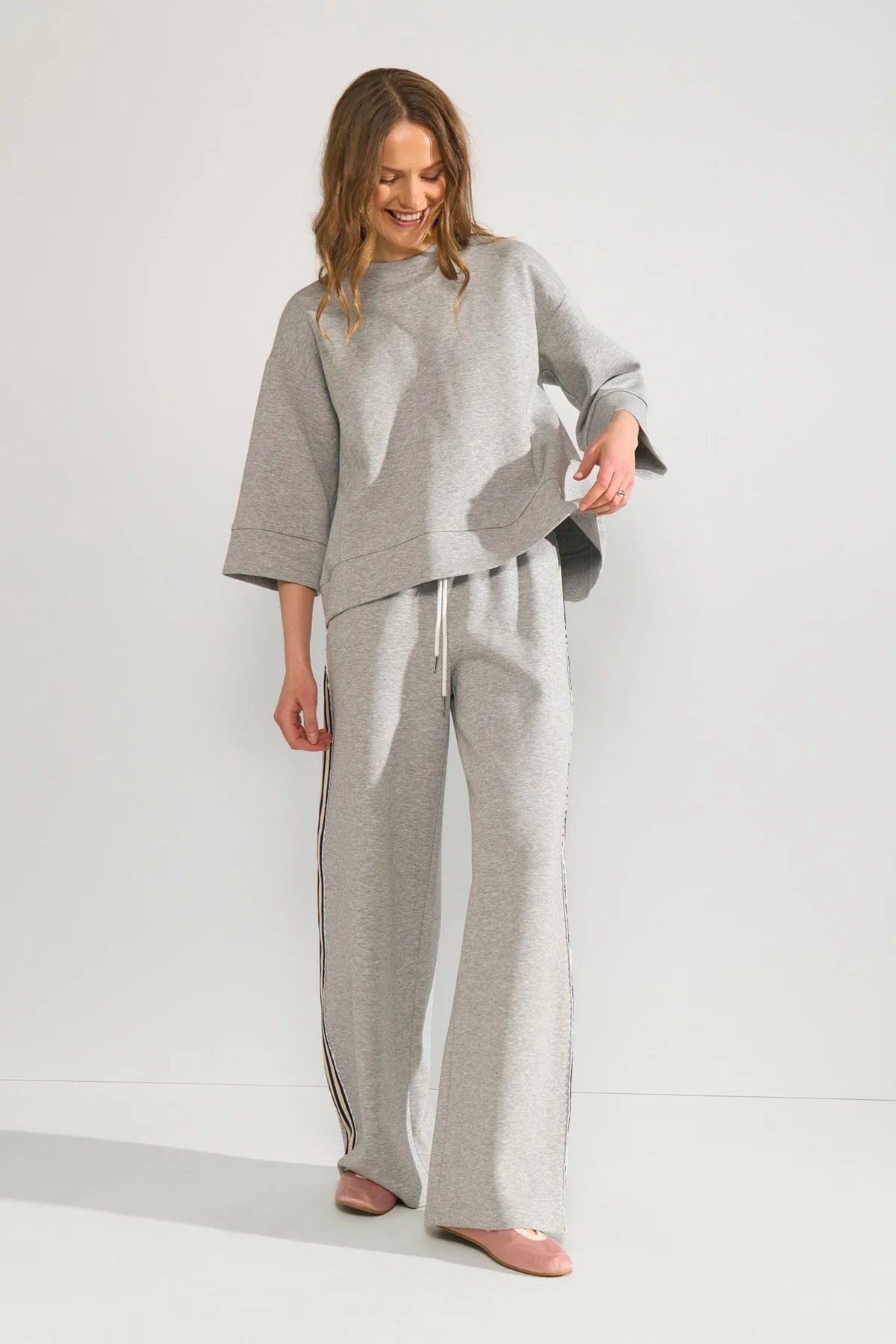 Model wearing grey joggers with a black embroidered striped outer seam on a neutral background