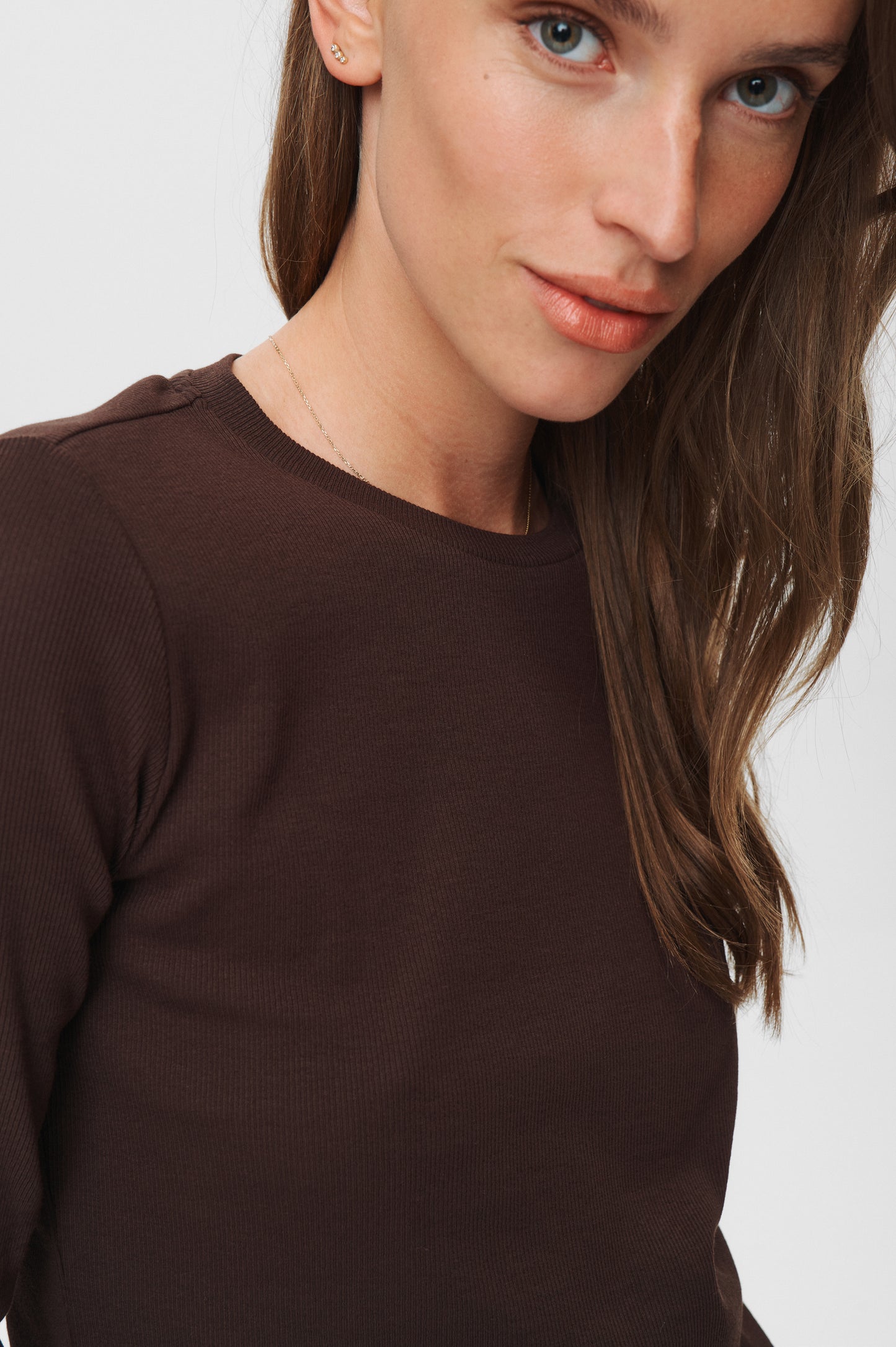 Woman wearing a brown long-sleeve top against a white background
