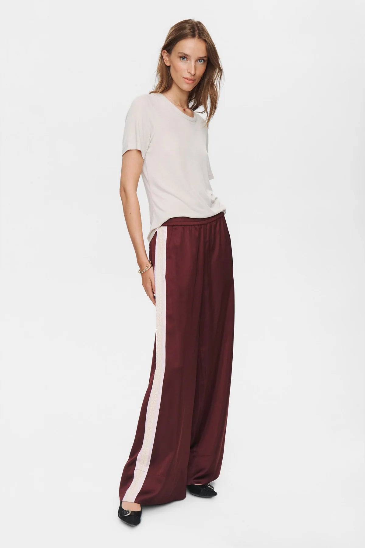 Woman wearing a white top and burgundy pants with a white stripe on a white background