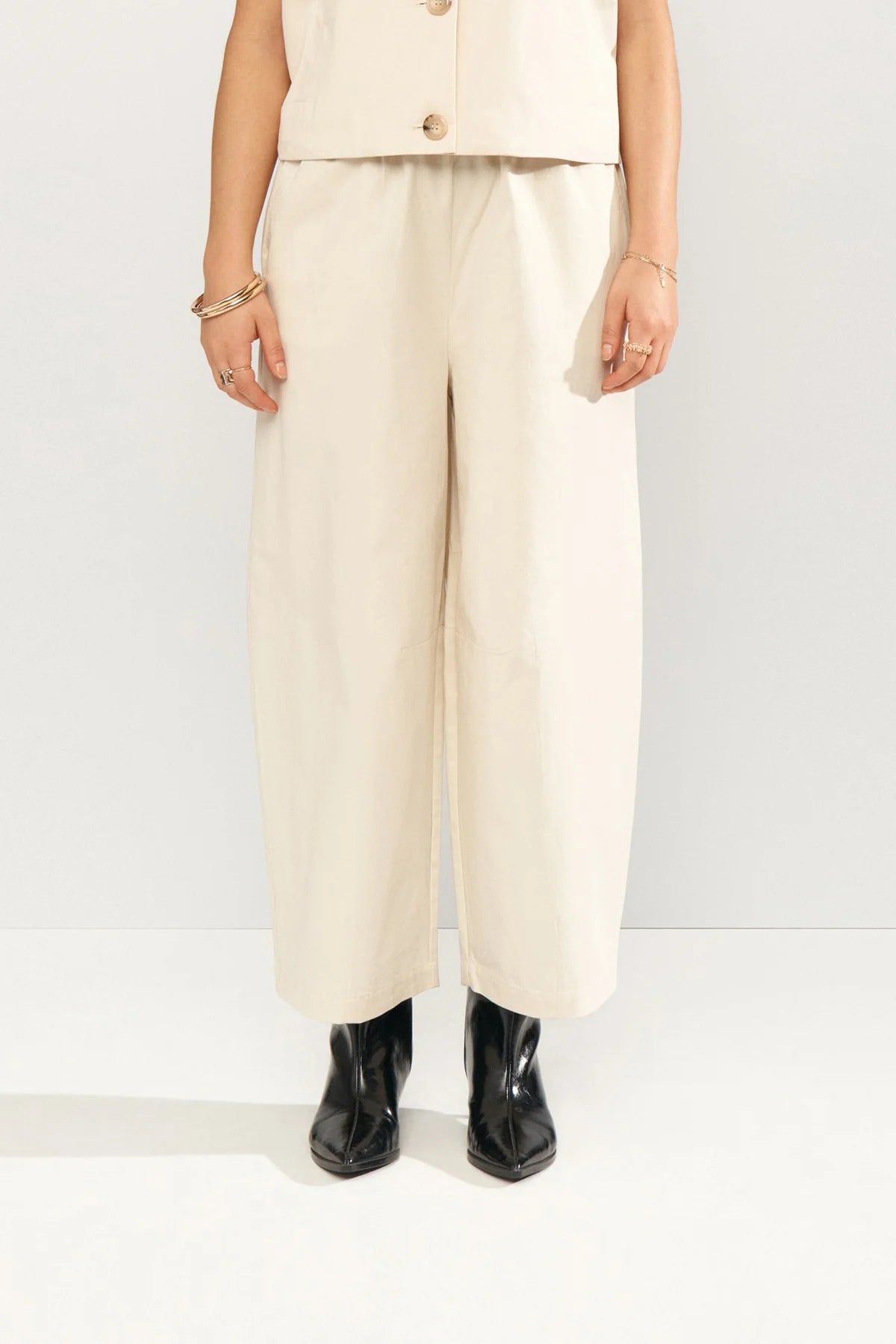 Person wearing a beige suit with wide-leg pants and black boots on a white background