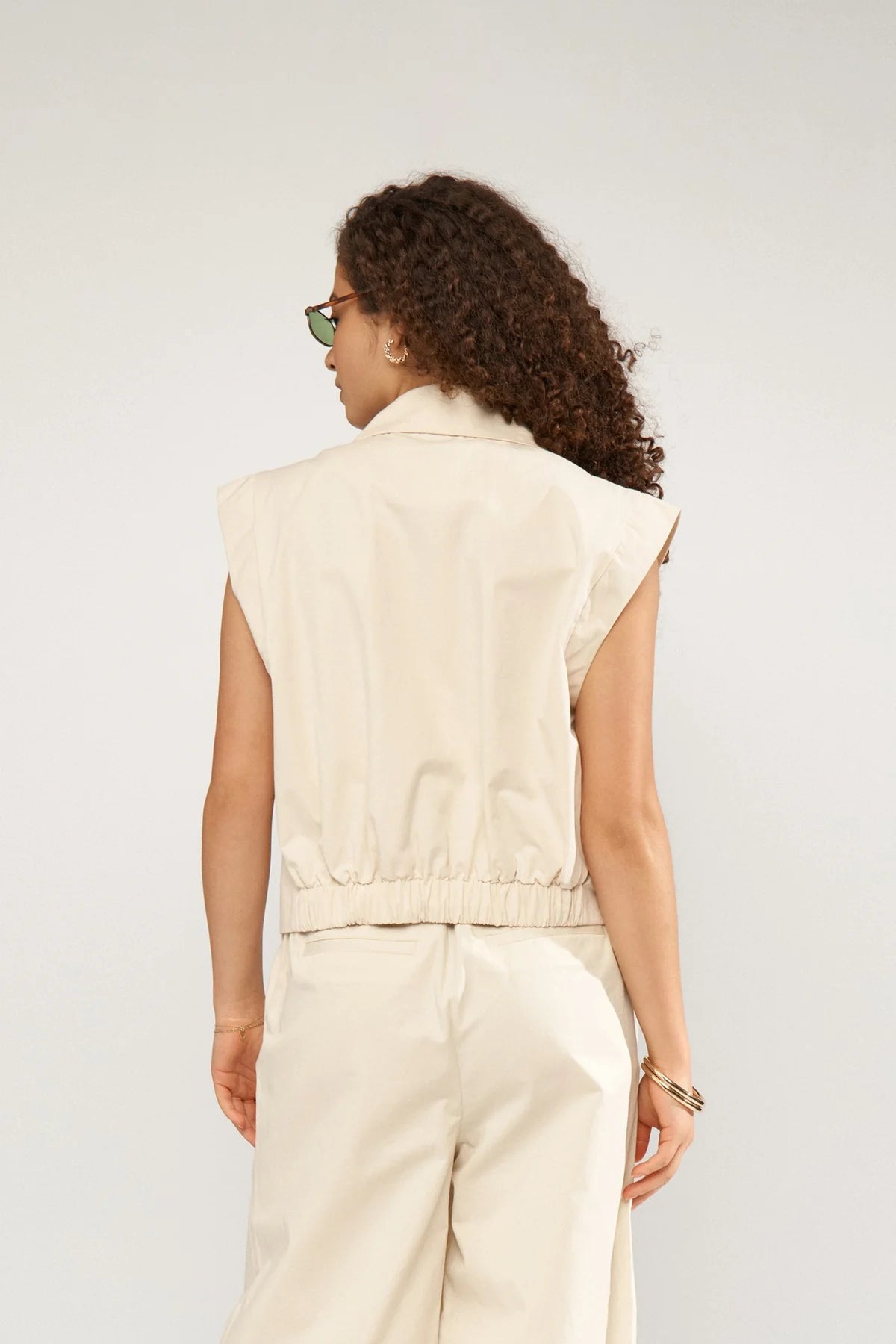 Woman wearing a beige sleeveless top and pants against a white background