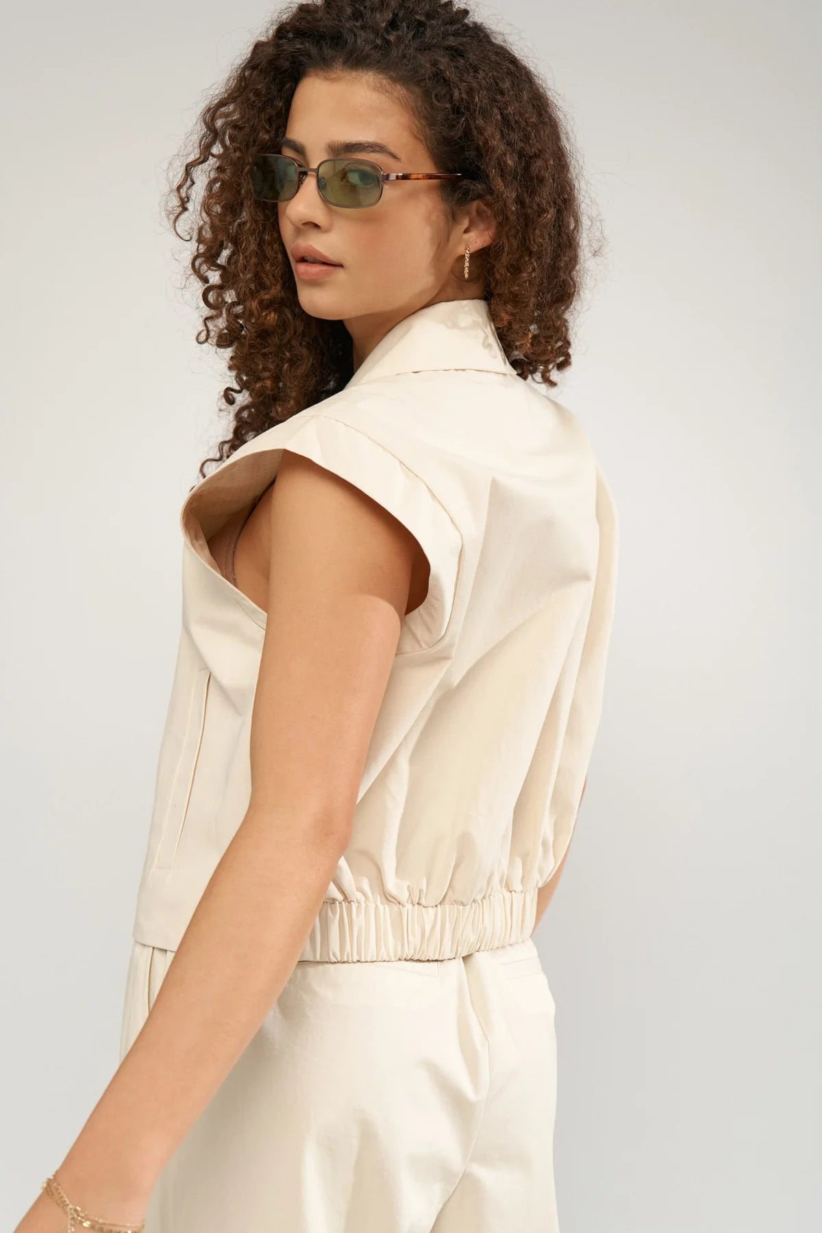 Woman wearing a beige sleeveless top and pants against a plain background