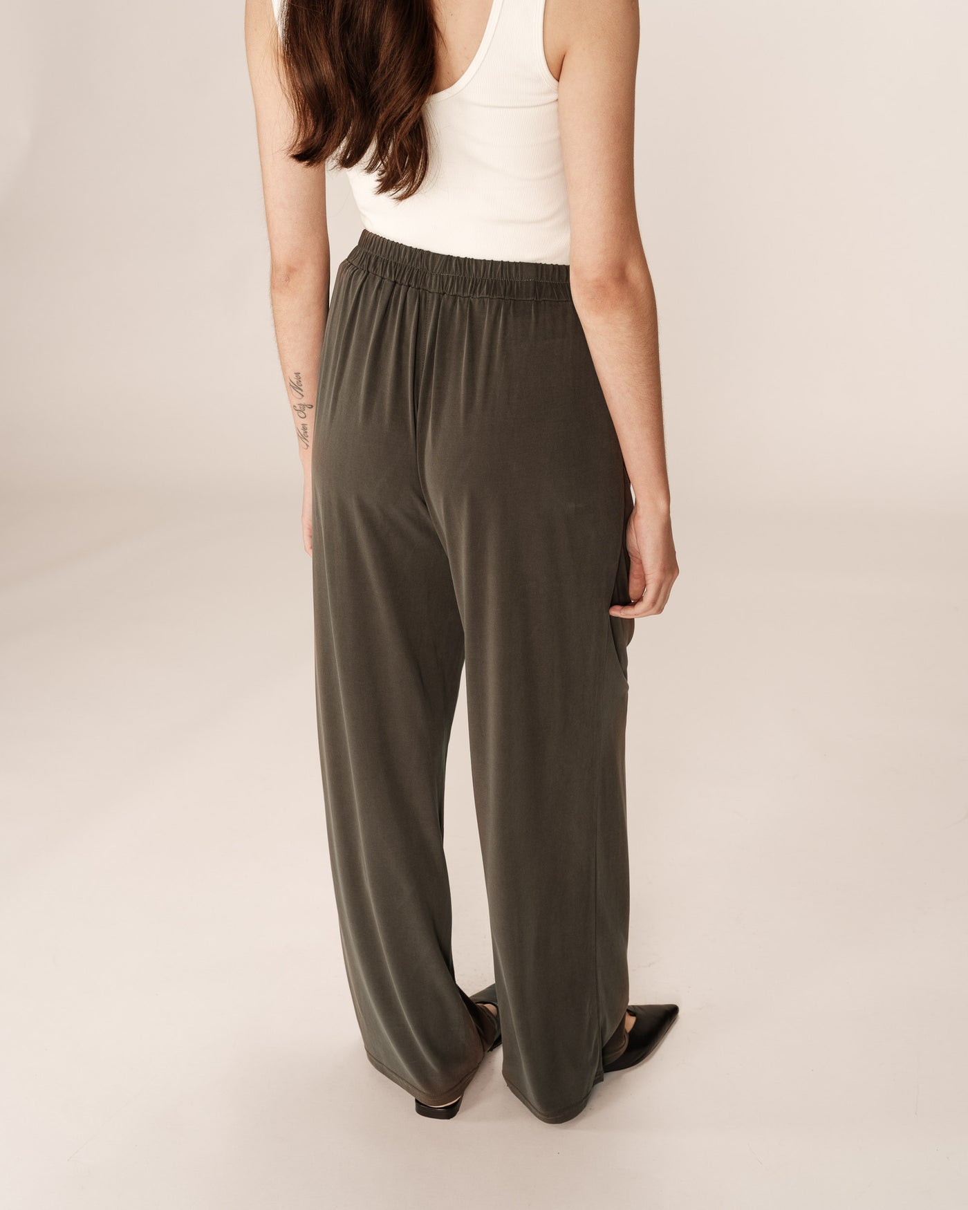Person wearing olive green wide-leg pants and a white top on a plain background