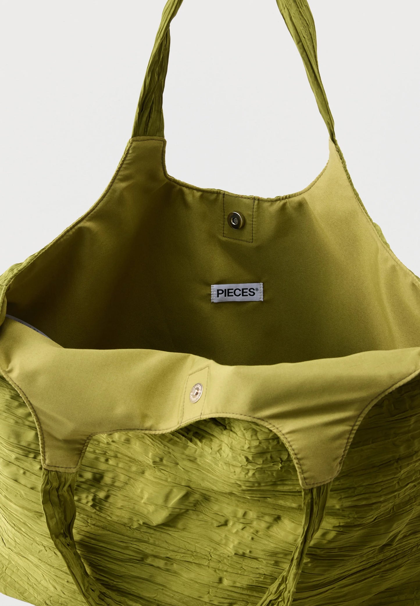 Close-up of the interior of a large olive green tote bag with a visible PIECES brand label, showing the fabric texture and snap-button closure.