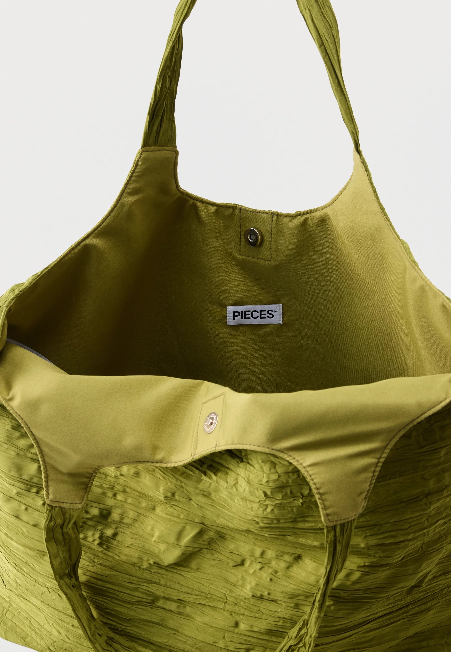 Close-up of the interior of a large olive green tote bag with a visible PIECES brand label, showing the fabric texture and snap-button closure.